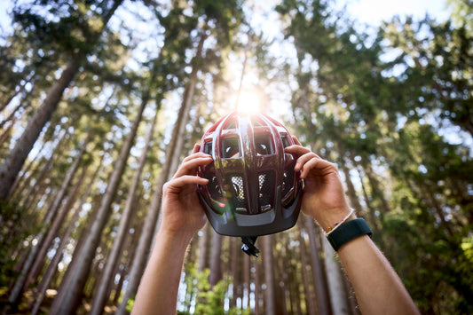Hände halten einen Fahrradhelm im Wald gegen das Licht und prüfen die Helmschale.